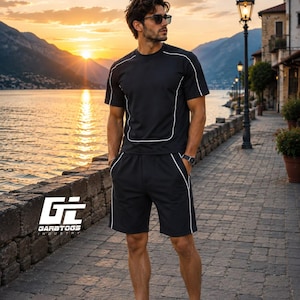 May include: A black short-sleeved t-shirt and matching black shorts set featuring thin white piping accents along the seams. The shirt has a crew neckline and the shorts include side pockets. The logo GI GARBTOGS INDUSTRY is visible.