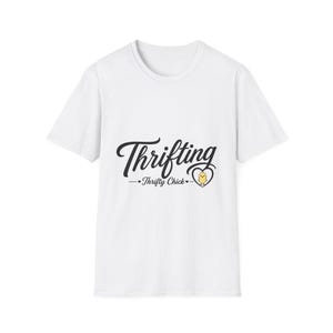May include: A white short-sleeved t-shirt featuring black text that reads Thrifting and Thrifty Chick, accompanied by a small yellow chick graphic enclosed within a black heart outline centered on the front of the garment.