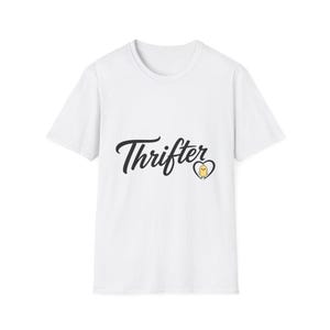 May include: A white short-sleeved t-shirt featuring the black text Thrifter in a cursive script font. To the right of the text is a small yellow chick illustration enclosed within a black heart outline centered on the chest of the garment.