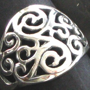 May include: A silver ring with a filigree design. The ring is made of a single piece of metal and has a smooth, polished finish.