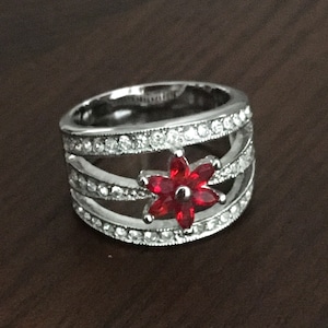 May include: A silver ring with a red flower design. The ring has three bands of clear stones.