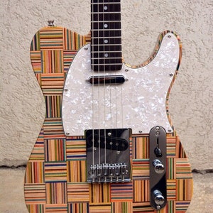 May include: A custom-made electric guitar with a body made of recycled skateboard wood. The guitar has a white pickguard and a black pickup. The guitar is on a black stand.