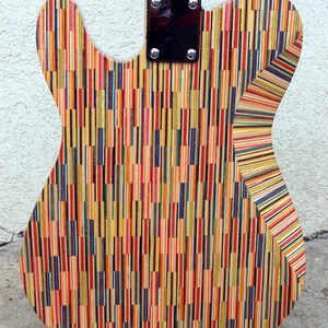 May include: A colorful electric guitar with a unique design. The back of the guitar is made from vertical strips of wood in various colors, including red, yellow, blue, and green. The neck is light-colored wood, and the hardware is black.