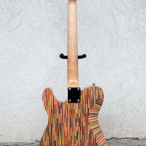 May include: A custom electric guitar with a body made from colorful, vertically-aligned wood strips. The neck is light-colored wood, and the headstock features silver tuning pegs. The guitar is displayed on a black stand.