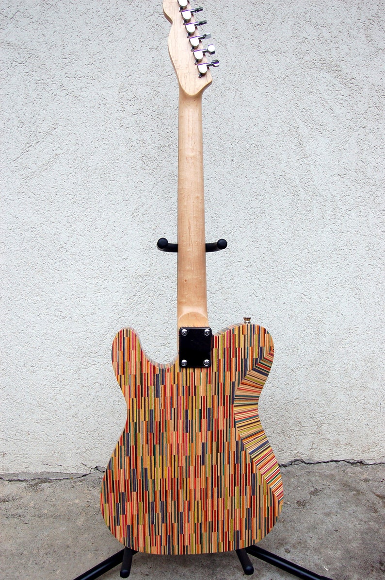 May include: A custom electric guitar with a body made from colorful, vertically-aligned wood strips. The neck is light-colored wood, and the headstock features silver tuning pegs. The guitar is displayed on a black stand.