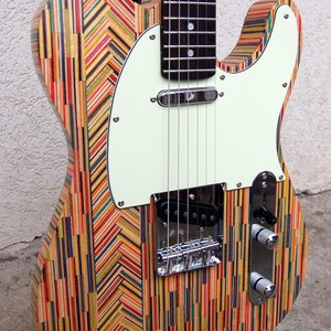 May include: A colorful electric guitar with a unique body made from recycled skateboard decks. The body features a vibrant pattern of vertical and angled stripes in various colors. The guitar has a white pickguard and chrome hardware.