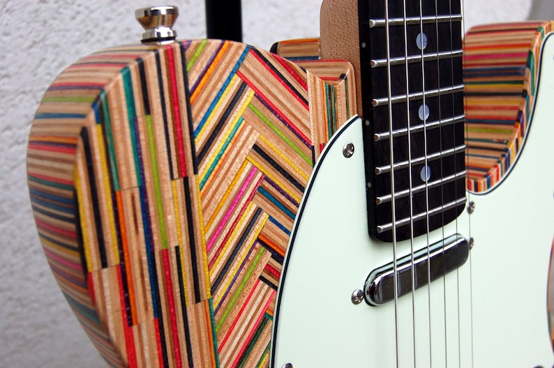 May include: A colorful electric guitar with a body made from layered wood, featuring a mix of vibrant colors. The guitar has a white pickguard, a black fretboard, and chrome hardware. The design is unique and eye-catching.