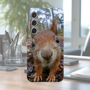 May include: A rectangular smartphone case featuring a high-resolution, close-up photograph of a brown squirrel with large black eyes and visible whiskers. The squirrel is positioned in the center, set against a blurred outdoor forest background.