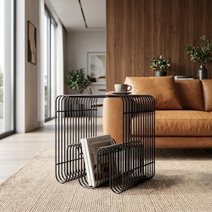 May include: A black metal side table featuring a series of vertical wire rods forming a square frame with an integrated magazine rack at the base. The top surface holds a small ceramic cup and saucer, while a magazine is stored in the lower section.