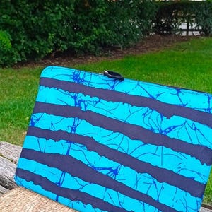 May include: A rectangular laptop sleeve featuring a vibrant cyan blue and black horizontal striped pattern with a crackled texture effect. The sleeve has a black zipper closure along the top edge and a slim, flat profile for carrying electronic devices.