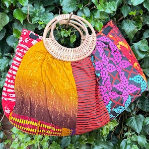 Puede incluir: Un bolso de tela acolchada con un diseño de patchwork en colores vibrantes que incluyen amarillo mostaza, rojo oscuro, negro y rosa brillante con un patrón de puntos geométricos. El bolso tiene dos asas circulares de ratán tejido claro.