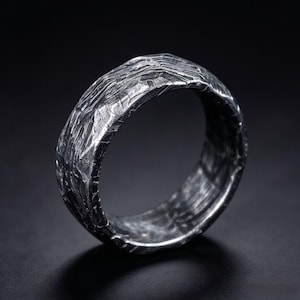 May include: A silver-toned ring featuring a highly textured, rugged surface with deep grooves and ridges that wrap around the entire band. The metal has a dark, oxidized finish that highlights the intricate, uneven patterns across the exterior.