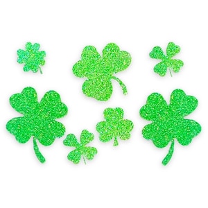 May include: Seven green glitter shamrock stickers. The shamrocks are different sizes and are arranged in a random pattern.