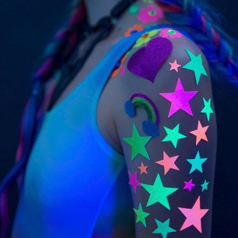 Colorful neon star stickers on arm of girl in white tank top. Profile view.