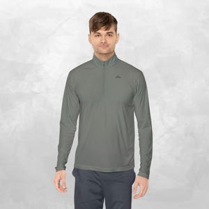 May include: A long-sleeved, quarter-zip pullover shirt in a solid olive-grey colour. The garment features a high collar with a small zip closure at the neck and a small black logo printed on the upper left chest area. The fabric appears smooth.