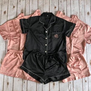 May include: Three pairs of pajamas, one black with white trim and the initials "ATL" embroidered on the chest, and two in a light pink color. All three pairs have short sleeves and shorts.