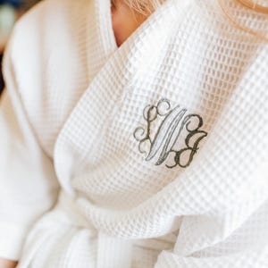 A close-up view of a person wearing a white bathrobe with a monogrammed logo on the front.