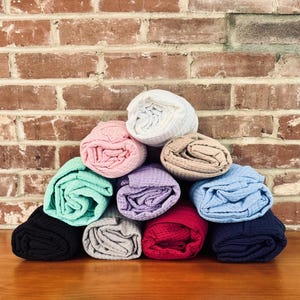 A pyramid-shaped stack of rolled-up towels in various colors, including blue, green, pink, and purple, against a brick wall.