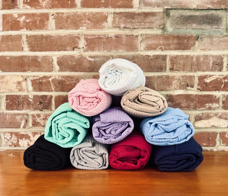 A pyramid-shaped stack of rolled-up towels in various colors, including blue, green, pink, and purple, against a brick wall.