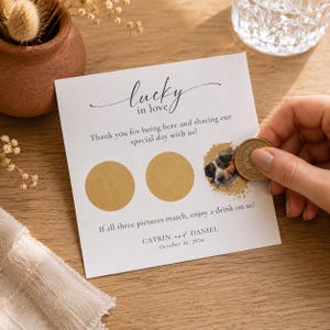 Puede incluir: Una tarjeta cuadrada blanca con el texto Lucky in love, Thank you for being here and sharing our special day with us!, y If all three pictures match, enjoy a drink on us!. Incluye tres círculos dorados para rascar y los nombres Catrin y Daniel.