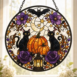 May include: A circular stained glass suncatcher featuring two black cats sitting beside two orange pumpkins. The design includes a crescent moon, stars, a bat, three white ghosts, purple flowers, and a lantern, all framed in a black metal border.