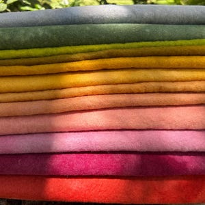 May include: A stack of twelve rectangular felt fabric sheets arranged in a gradient color sequence. The colors transition from light gray at the top, through shades of olive, yellow, orange, and pink, to a vibrant red at the bottom edge.