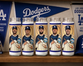 May include: Five clear glass prayer candles featuring illustrated baseball players in Los Angeles Dodgers uniforms. Each candle displays a player wearing a blue cap and holding a scroll. The candles are arranged in a row on a wooden surface.