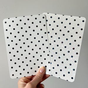 May include: Two rectangular cards with rounded corners. The left card is white with a repeating pattern of solid black polka dots. The right card features a white background with black polka dots and a holographic finish that reflects light.