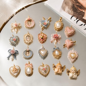 May include: A collection of twenty decorative jewellery charms featuring various designs including hearts, bows, cameos, and cherubs. The charms are crafted with gold-tone metal accents, pastel-coloured enamel, faux pearls, and miniature floral details.