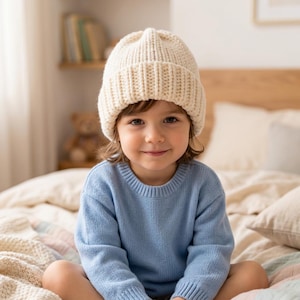 May include: A cream-coloured, chunky knit beanie with a wide, ribbed cuff. The hat features a thick, textured yarn construction with a classic folded brim design, providing a simple and functional head covering that sits snugly on the head.