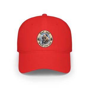 May include: A bright red baseball cap featuring a circular graphic on the front. The design depicts a bison in a snowy landscape with a small bird perched on its back, surrounded by the text Get out While you can in a circular border.