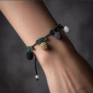 May include: A crochet bracelet featuring small, multi-coloured tulip-shaped charms in black, gold, grey, and white, attached to a thin black cord with green crocheted leaves. The text "Crochet Tiny Tulip Bracelet Pattern" and "Instant PDF Download" is visible.