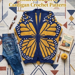 May include: A crochet cardigan featuring a monarch butterfly wing pattern in yellow, navy blue, and white. The garment is displayed alongside blue jeans, a wristwatch, a book titled The Crocheter's Almanack, and a ball of yellow yarn with a hook.