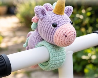 May include: A crochet unicorn slap bracelet buddy with a lavender head, pink snout, gold horn, and mint green band. The text reads: Crochet Unicorn Slap Bracelet Buddy Pattern and Instant PDF Download. The unicorn has black eyes and a colorful mane.