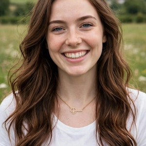 May include: A gold-toned metal necklace featuring a delicate script pendant that spells out the word Dios. The pendant is attached to a thin, matching gold-colored chain that rests against a plain white t-shirt worn by a person with long brown hair.
