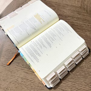 May include: An open Bible with cream-colored pages, featuring printed text, lined margins for notes, and a series of labeled index tabs along the side. The tabs include visible text such as Proverbs, Jeremiah, Isaiah, Song of Solomon, and Ecclesiastes.
