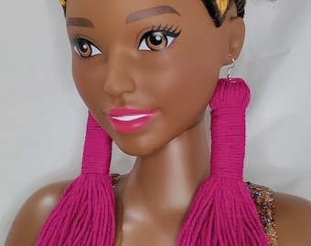 Può includere: Una bambola con la pelle marrone e un'ampia acconciatura afro con riflessi biondi indossa lunghi orecchini a nappa rosa.
