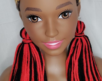 Puede incluir: Cabeza de maniquí con piel marrón oscuro, ojos marrones y labios rosados. El maniquí tiene un peinado rizado con cabello castaño oscuro, rubio y castaño claro. Lleva pendientes de hilo rojo y negro.