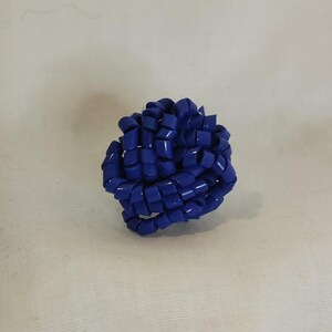 May include: A vibrant blue, spherical decorative object. The object is composed of numerous looped, rectangular segments, creating a textured, interwoven design. The overall shape is round, with a glossy finish.