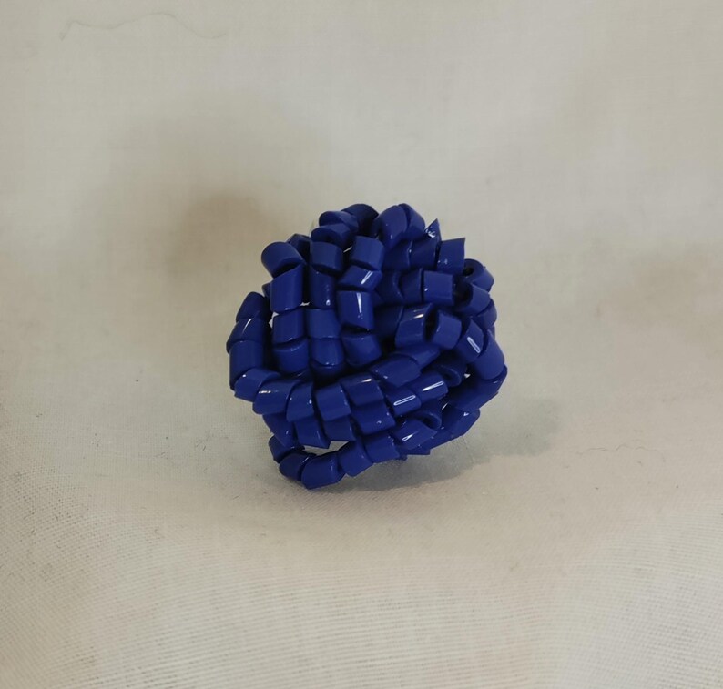 May include: A vibrant blue, spherical decorative object. The object is composed of numerous looped, rectangular segments, creating a textured, interwoven design. The overall shape is round, with a glossy finish.