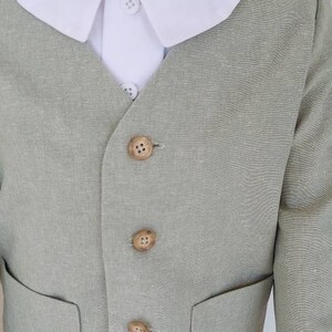 May include: A light green linen suit with a white collared shirt. The suit has a button-up front and a pocket on each side. The buttons are made of wood.