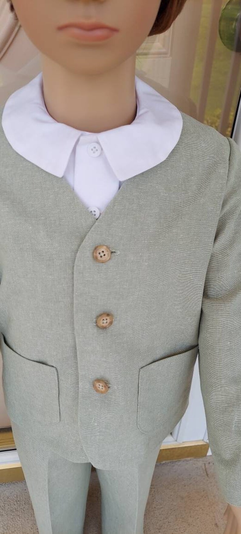 May include: A light green linen suit with a white collared shirt. The suit has a button-up front and a pocket on each side. The buttons are made of wood.