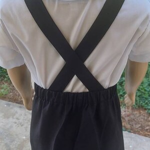 May include: A white collared shirt with black suspenders and black shorts. The suspenders are crossed in the back.