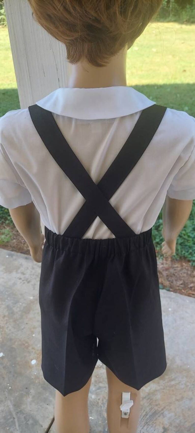 May include: A white collared shirt with black suspenders and black shorts. The suspenders are crossed in the back.