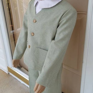 May include: A light green suit for a child. The suit has a collared shirt, a jacket with three buttons, and pants with a pocket.