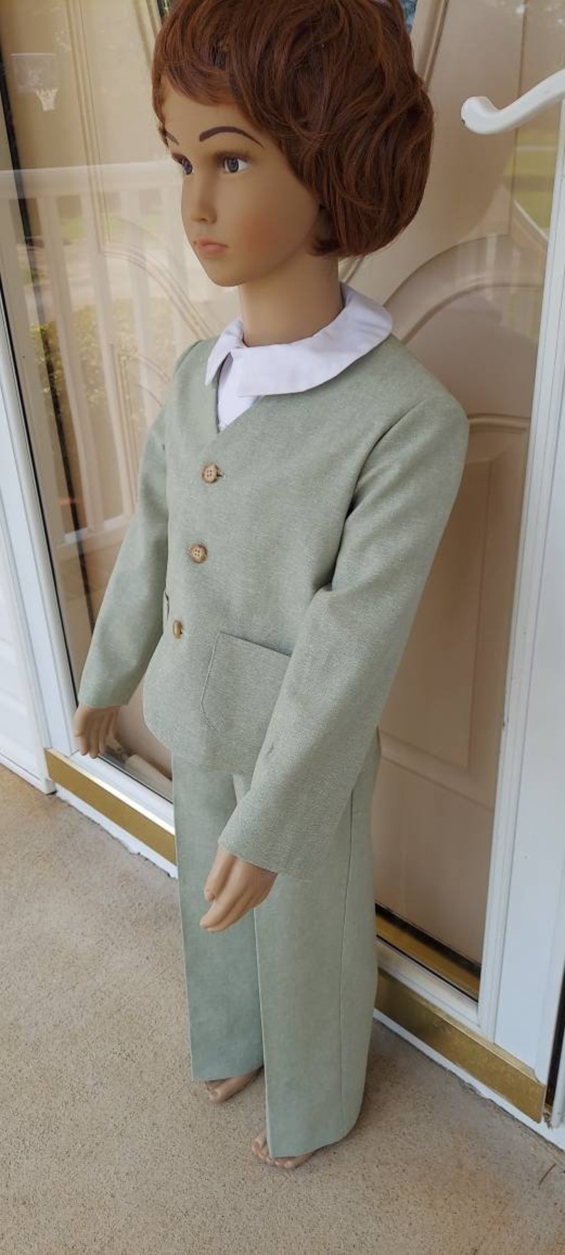 May include: A light green suit for a child. The suit has a collared shirt, a jacket with three buttons, and pants with a pocket.