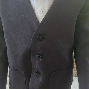 May include: A black suit with a white collared shirt. The suit has a vest with four buttons and two pockets. The suit is worn by a child.