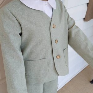 May include: A light green suit with a white collared shirt. The suit has a jacket with a pocket and buttons. The pants are long and have a straight leg.