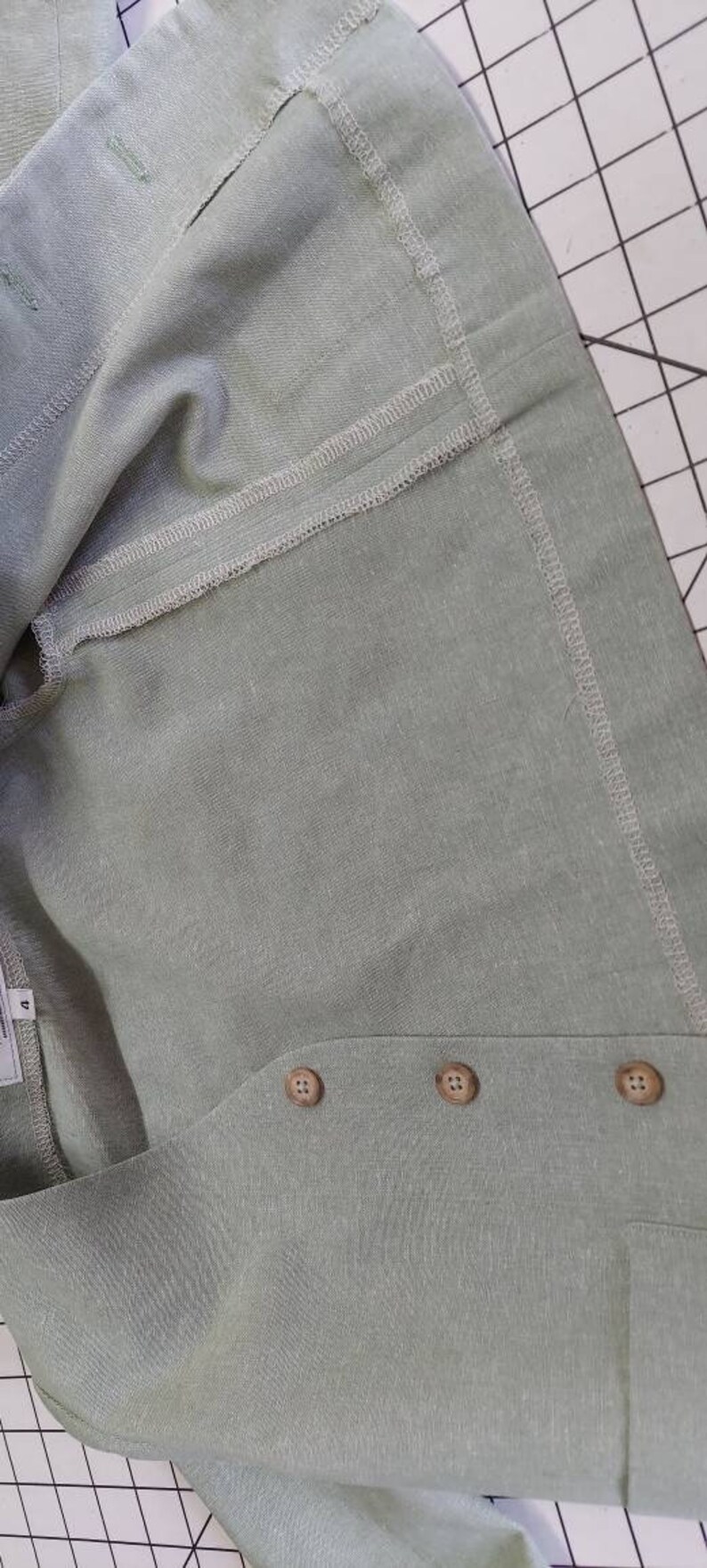 May include: A light green linen garment with three brown buttons. The garment has a seam down the center and a folded edge.