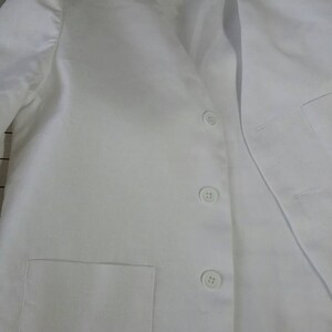May include: White blazer with a v-neck and four buttons. The blazer has a pocket on the left side and a label that says "Nanny B's".